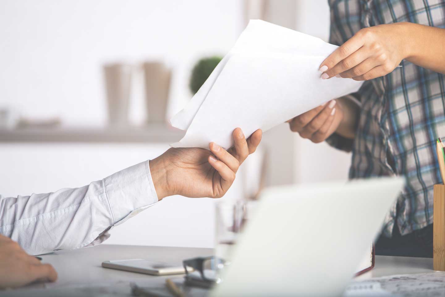 People handing a document to each other with a laptop.